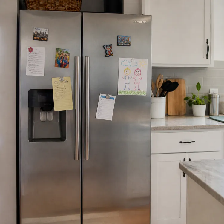 Stainless steel refrigerator with magnets and notes in a modern kitchen with white cabinets