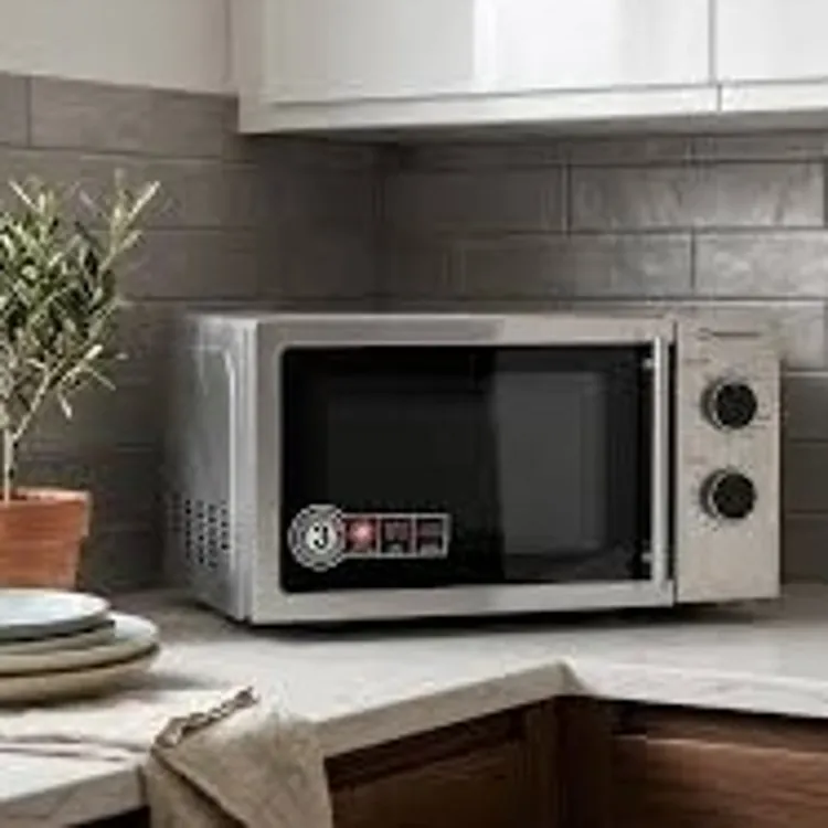 A microwave oven on a kitchen countertop near a potted plant and stacked plates