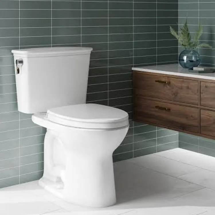 A white toilet next to a wooden vanity in a bathroom with green tile walls.