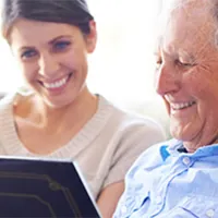 elderly man looking through book with young woman