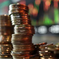 stack of coins in front of stock exchange display
