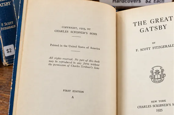 Open first edition copy of The Great Gatsby by F. Scott Fitzgerald next to another copy on a shelf