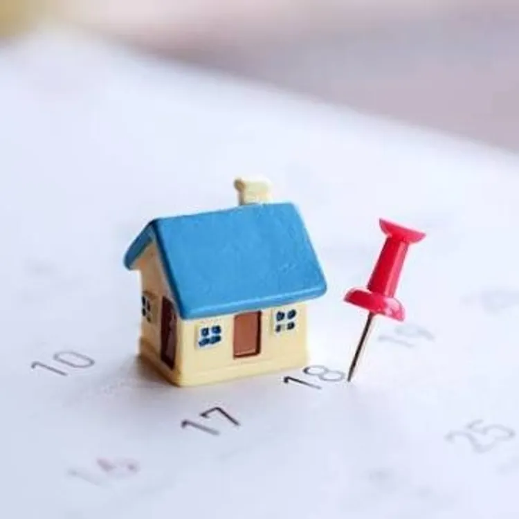 Miniature house and red pushpin placed on a calendar page