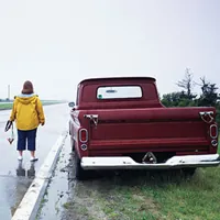 rear view of a woman standing near a truck while holding jumper cables