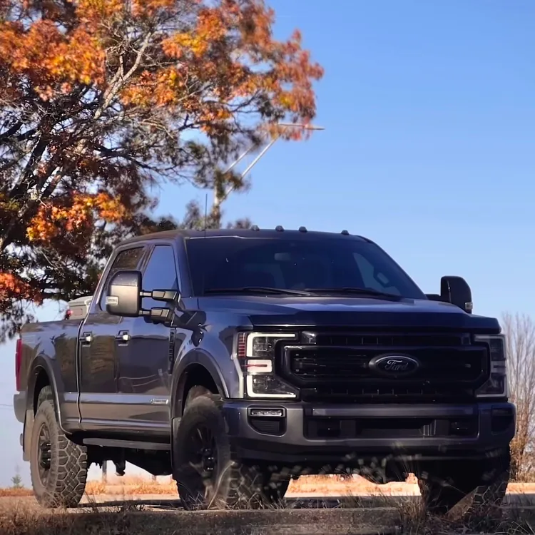 Black pickup truck parked on a grassy area with autumn trees and a clear blue sky in the background.