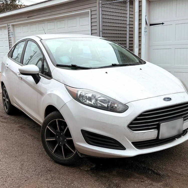 White compact car parked in a residential driveway with garages in the background.