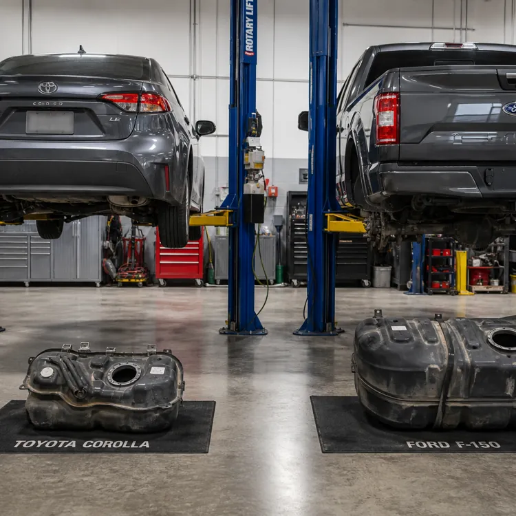 Toyota Corolla and Ford F-150 vehicles on lifts in a garage with their fuel tanks removed and placed below