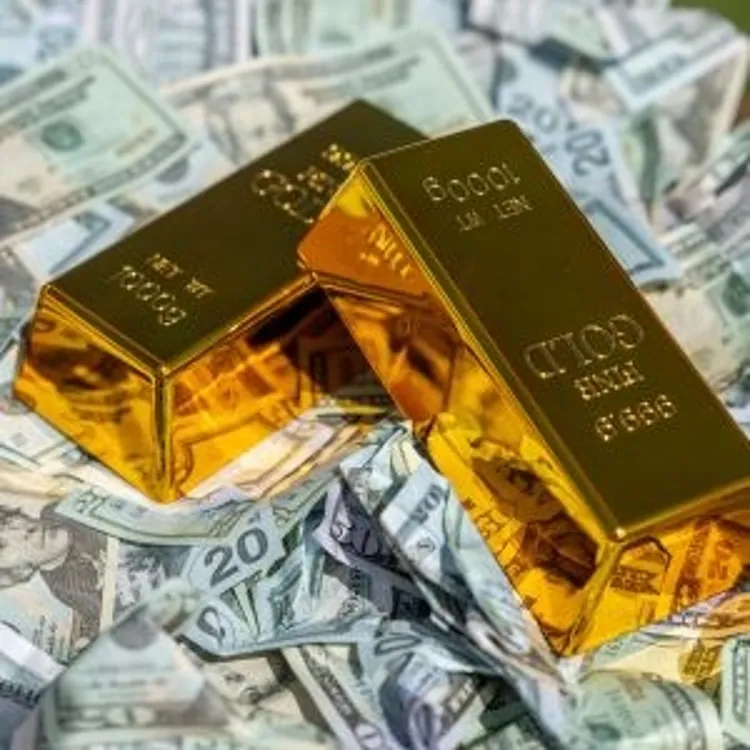 Two gold bars resting on a pile of assorted US dollar bills