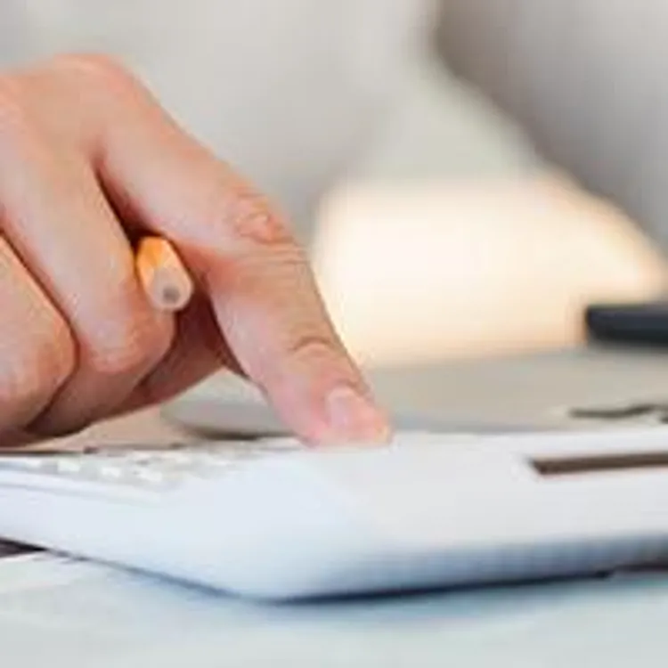 hand typing on calculator with model house in front