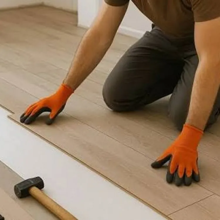 Person wearing orange gloves installing wooden flooring with tools on the floor