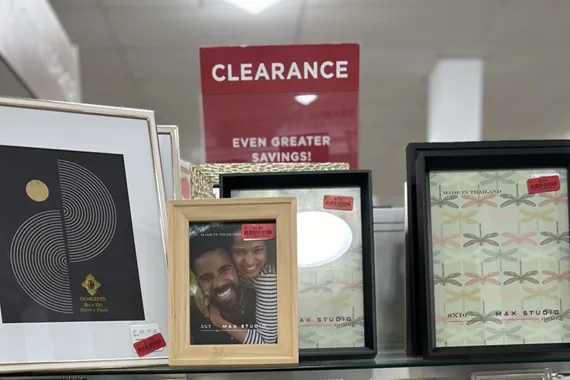 Assorted picture frames with red clearance price tags displayed on a store shelf under a clearance sign
