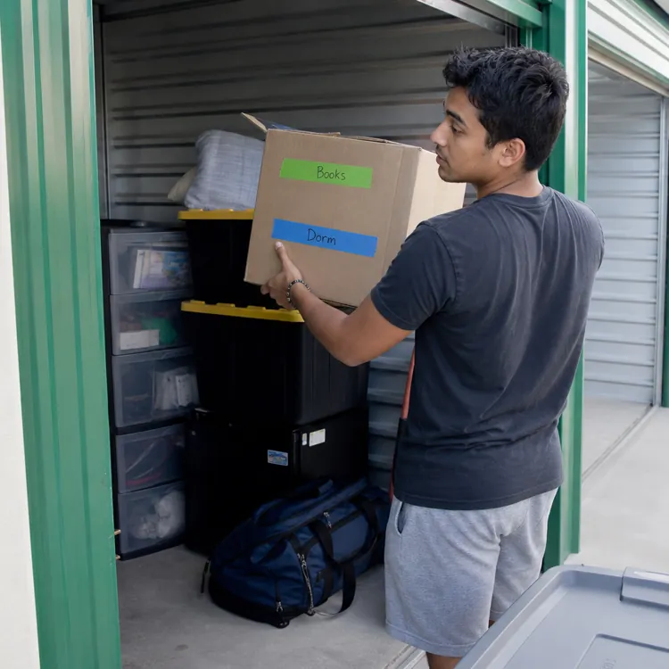 Young man placing labeled box into a storage unit with plastic bins and bags inside