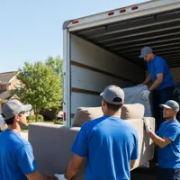 Four movers in blue uniforms loading furniture into a moving truck in a suburban neighborhood.