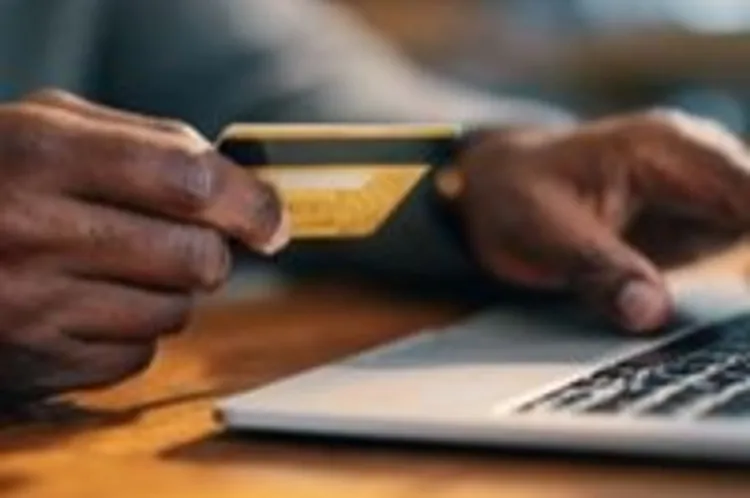 a man seated at his laptop with a credit card in hand