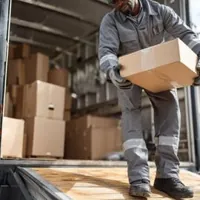 a person in a gray uniform and gloves unloading a cardboard box from a delivery truck