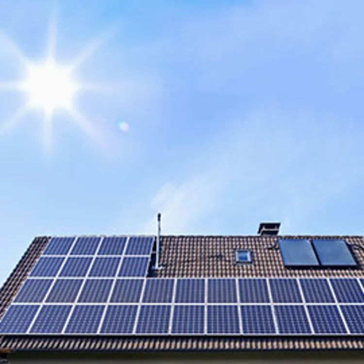 solar panels on houseroof in front of blue sky with sun