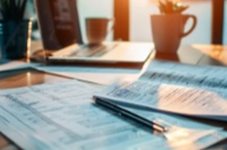 tax forms in the foreground and a laptop in the background on a table
