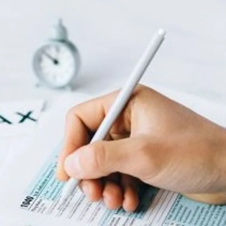Hand filling out tax forms with a pen on a white table