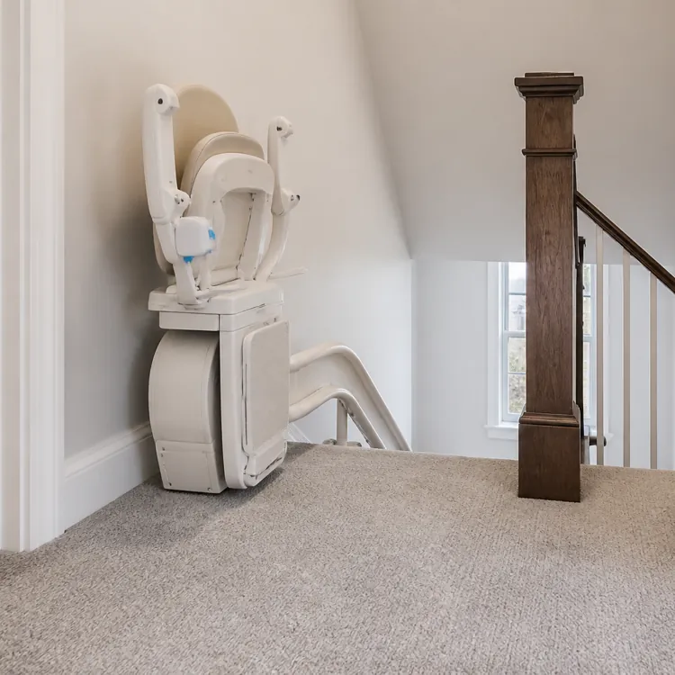Folded stairlift installed at the top of a carpeted staircase in a residential hallway