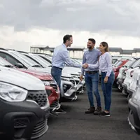 happy couple shaking hands with a salesperson in the middle of the car lot