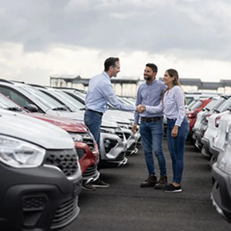 happy couple shaking hands with a salesperson in the middle of the car lot