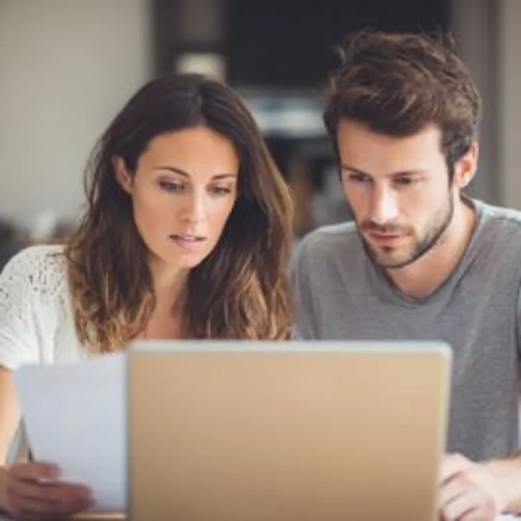 a man and woman looking intently at a document with their laptop open
