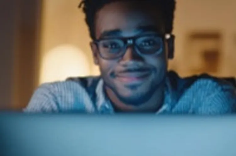 a male young adult smiling while looking at a computer monitor