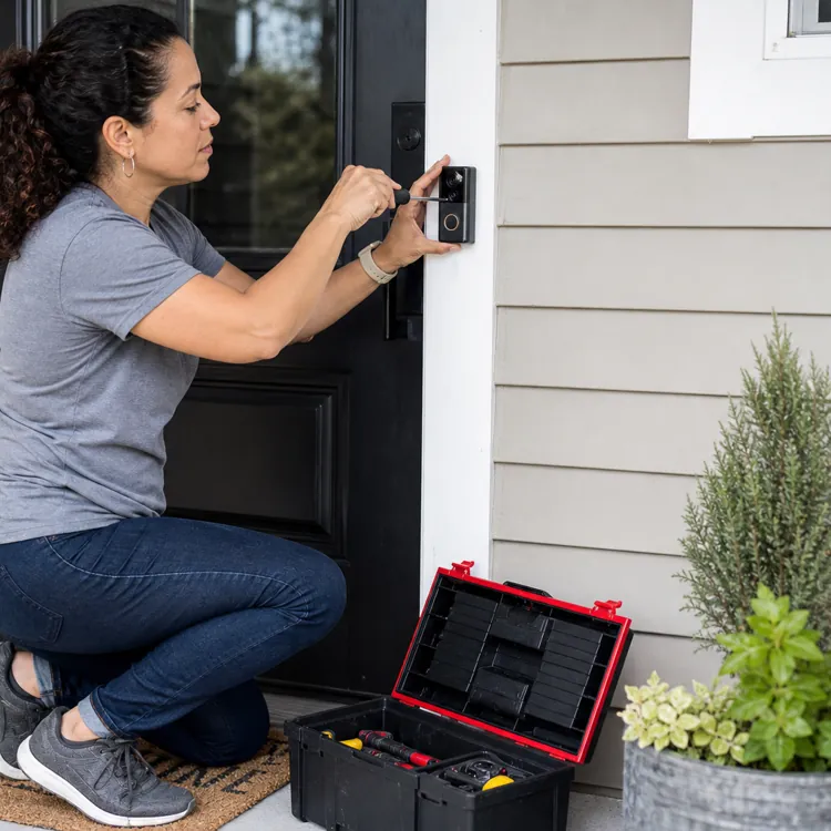 Woman installs a smart doorbell at a black front door with a toolbox nearby