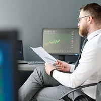 young adult man sitting at desk in office reviewing a piece of document