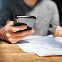 a man sitting while holding his cellphone and some documents