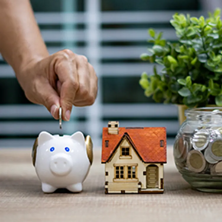 hand dropping coin to a piggybank next to a house figurine