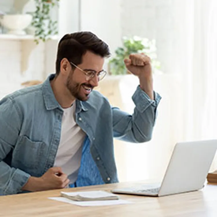 young man in spectacles overjoyed while reading good news on computer screen