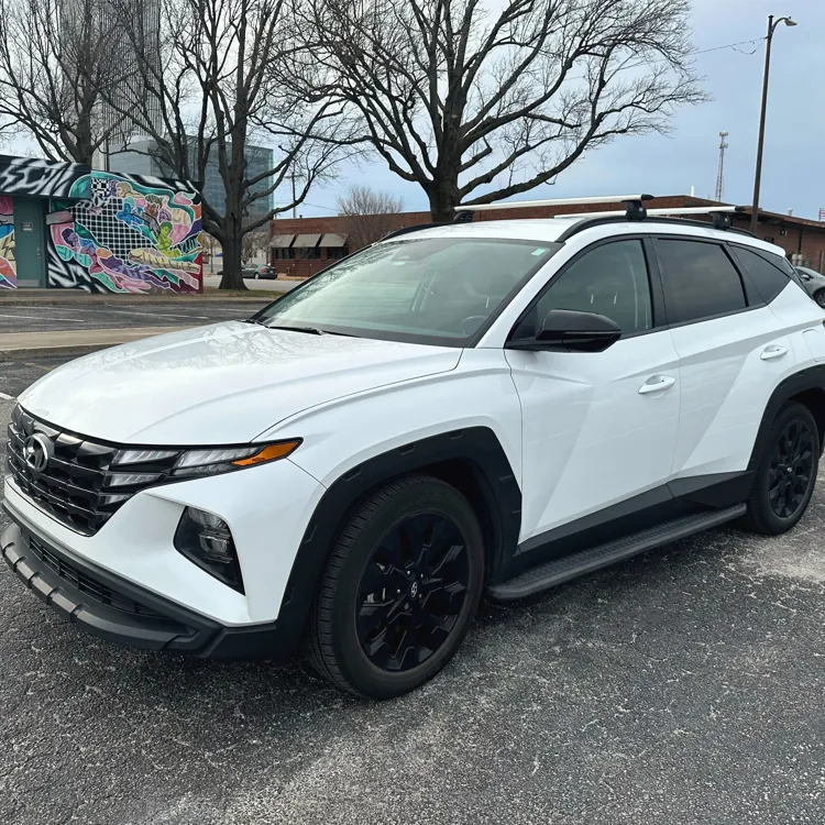 White SUV parked in an urban area with colorful graffiti on a nearby building and bare trees in the background.