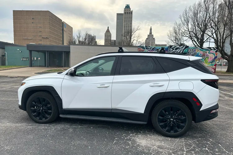 White SUV parked in an urban area with modern buildings and street art in the background under an overcast sky.