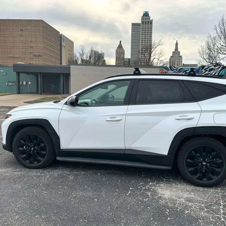 White SUV parked in an urban area with modern buildings and street art in the background under an overcast sky.