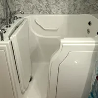 Walk-in bathtub with showerhead and marble-patterned walls, featuring a safety door and a shower curtain with ocean design.