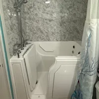 Walk-in bathtub with a showerhead and marble-patterned walls, featuring a partially open shower curtain.
