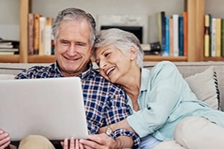 older couple sitting on a couch looking at a laptop