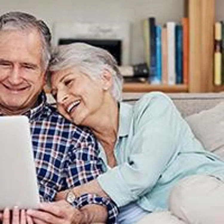 older couple sitting on a couch looking at a laptop
