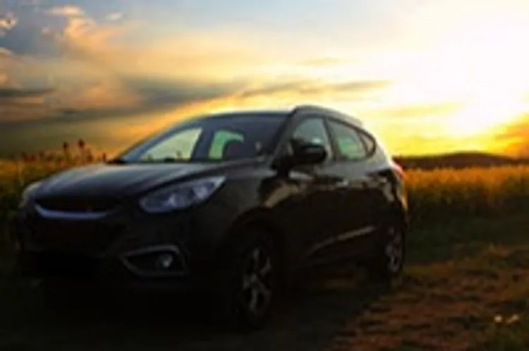car in a field with the sun setting in the background
