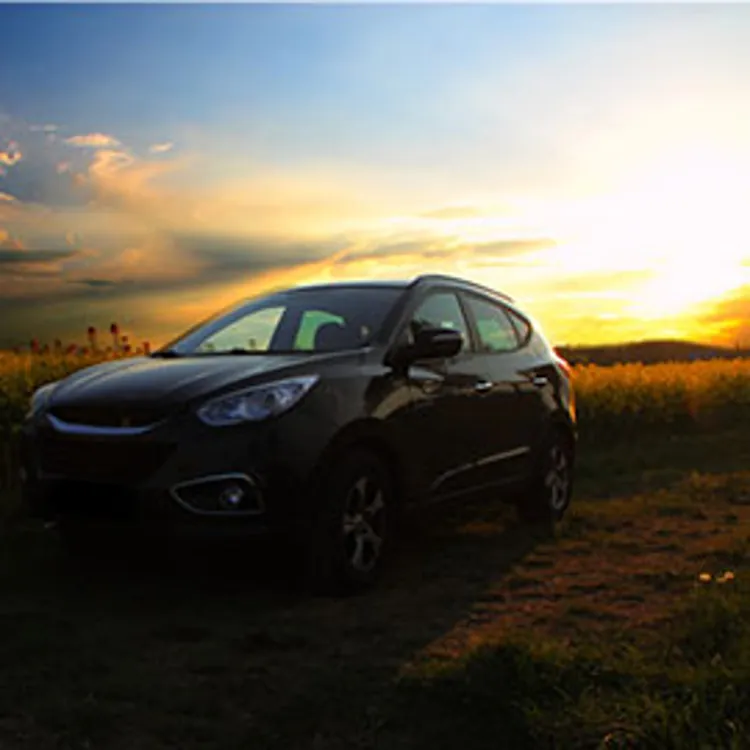 car in a field with the sun setting in the background