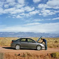 man looking under hood of car on desert road