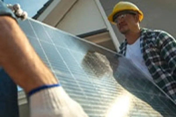 two men carrying solar panel onto construction site