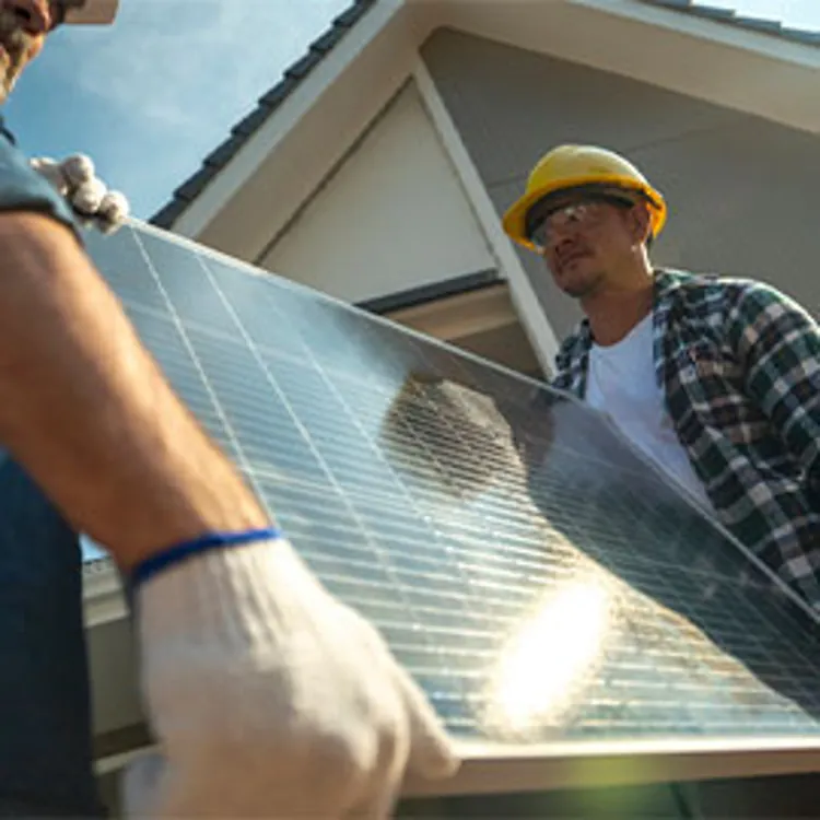 two men carrying solar panel onto construction site