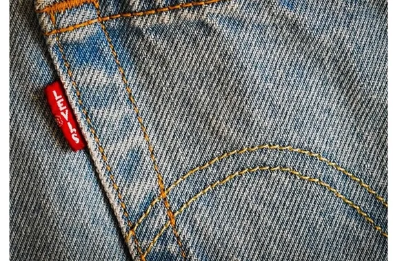Close-up of blue denim jeans pocket with orange stitching and a red brand tag