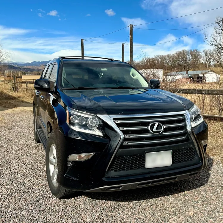 Black SUV parked on a gravel driveway with a rural landscape and blue sky in the background.