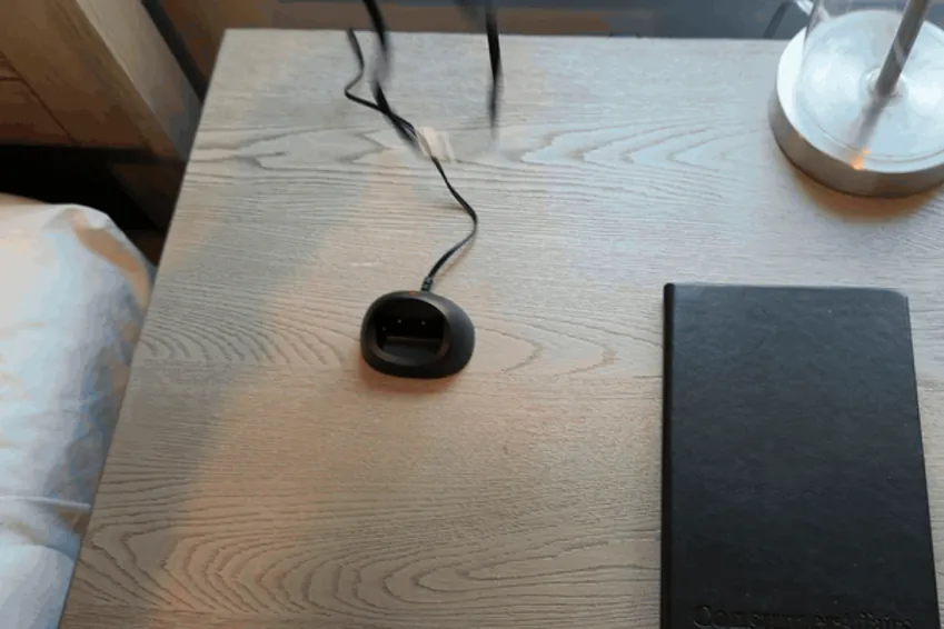 Hand setting the VIP X2 pendant into its charging dock on a bedside table until the red light comes on