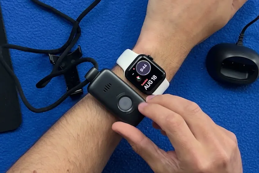 LifeFone VIP X2 pendant held on a wrist next to an Apple Watch for size