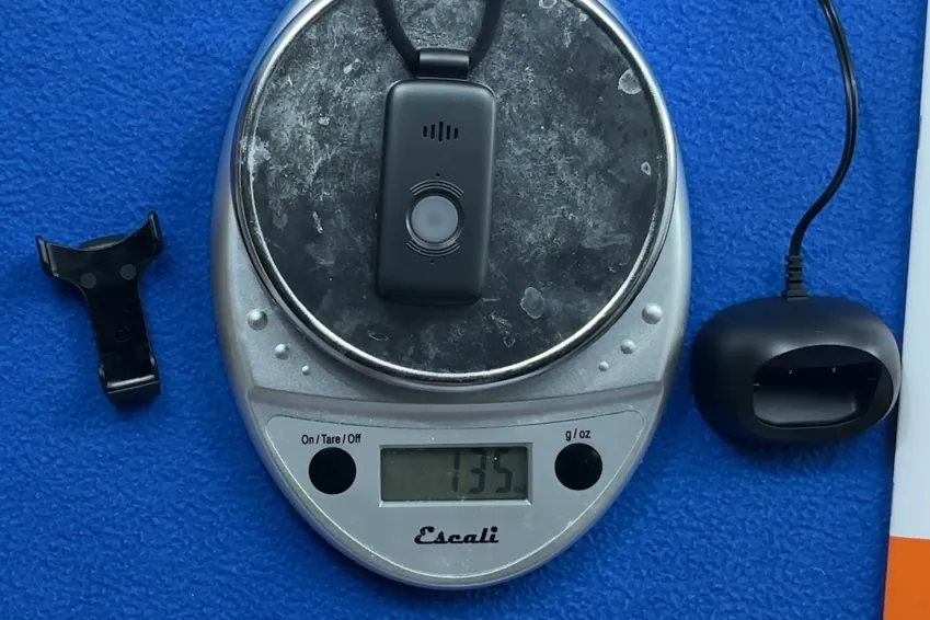 LifeFone VIP X2 pendant on a kitchen scale reading 1.35 ounces, next to its belt clip and charging dock