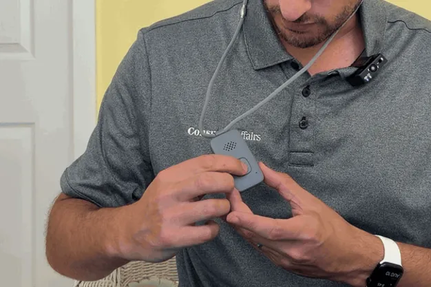 Thumb pressing the Lifeline On the Go pendant's help button until the light turns solid blue